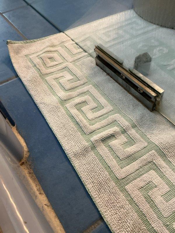 Responded to service call for malfunctioning glass shower door with faulty hinge/pivot point causing door to scrape bottom track. Inspected shower enclosure, identified worn pivot mechanism and misalignment issue at base of door frame. Documented existing conditions including visible corrosion at metal trim where door meets tile flooring.
