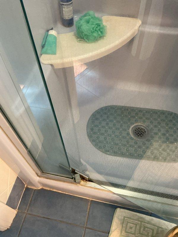 Responded to service call for malfunctioning glass shower door with faulty hinge/pivot point causing door to scrape bottom track. Inspected shower enclosure, identified worn pivot mechanism and misalignment issue at base of door frame. Documented existing conditions including visible corrosion at metal trim where door meets tile flooring.