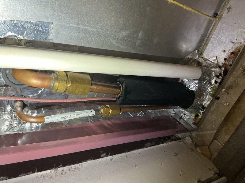 # After Hours Emergency HVAC Service

Responded to an after hours emergency call for HVAC system issues. Upon arrival, accessed the mechanical space and inspected the ductwork assembly and refrigerant line connections. Found compromised insulation and potential refrigerant line concerns in the confined crawlspace area. Documented existing copper piping configuration, brass compression fittings, and condensate drain line routing. Assessed the condition of thermal barriers and metallic insulation wrapping around primary refrigerant lines. Verified all pipe connections and fittings for proper installation and potential leak points. Photographed the installation for service records showing the white insulated refrigerant line, copper tubing with brass fittings, and surrounding ductwork assembly. System components were located in a tight access area with concrete flooring requiring careful navigation. Completed visual inspection of all accessible HVAC components and documented findings for 