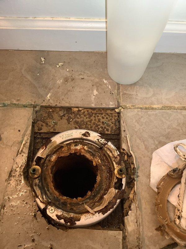 Responded to a call for a toilet leaking into the basement, confirmed by blue-tinted water visible below. Upon inspection, discovered a severely corroded and rusted toilet flange with significant deterioration at the floor connection point. Removed the toilet to access the damaged flange, replaced the failed flange with new hardware, installed a new wax ring seal, and properly re-set and secured the toilet to restore proper function and eliminate the leak.