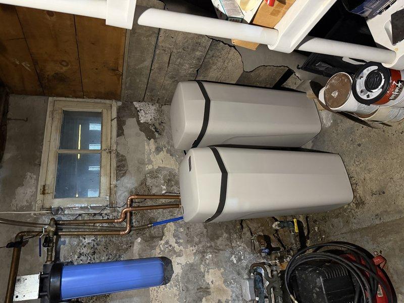 Completed installation of Hague water softener system in basement utility area per approved estimate. System installed with proper copper piping connections, blue filter housing, and dual white storage tanks secured with black strapping. All components tested and operational upon completion.
