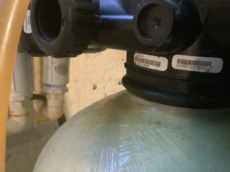Responded to customer complaint of squealing noise during regeneration cycle, sulfur odor in water, and slimy shower water. Inspected water softener system equipped with Smart Touch Control ST-200 during backwash cycle operation. Verified system regeneration schedule set for 10:30-11:00 PM as configured for household needs. Documented control valve assembly with barcode BND0355940, examined fiberglass tank condition, and checked plumbing connections. Photographed system components including control head, tank assembly, and PVC piping for service records.