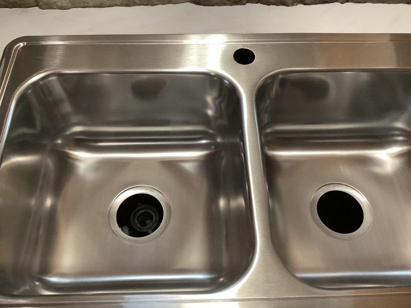Installed customer-provided kitchen faucet on newly installed countertop with double-basin stainless steel sink. Connected water supply lines and completed drain line installation, including integration of dishwasher drain connection to the system. All plumbing connections tested and verified for proper operation with no leaks detected.