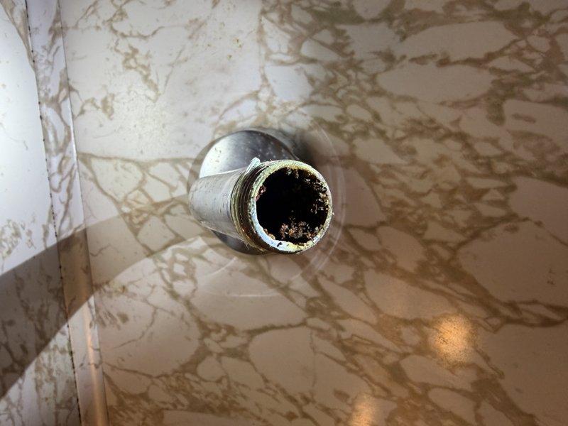 Responded to a clogged shower head issue where water flow remained restricted even after removing the fixture. Investigated the shower arm pipe and confirmed an internal blockage using a probe. Inspected the property's cast iron plumbing system and documented areas of concern, including deteriorated pipe sections in the basement area showing signs of age and potential corrosion. Photographed the clogged shower arm opening revealing significant mineral buildup and debris accumulation, as well as aging cast iron pipes with severely deteriorated paint indicating possible moisture exposure. Customer has access to an alternative upstairs shower during resolution of the issue.