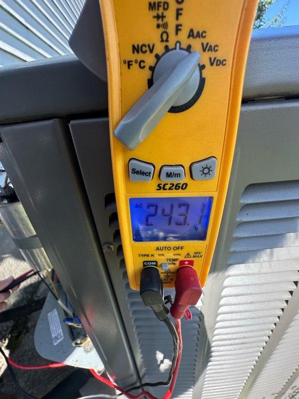 Completed preventive maintenance inspection on air conditioning system. Documented equipment with photographs of condensate drain assembly showing P-trap, flexible drain lines, and associated plumbing components in proper working condition. Verified system electrical parameters using digital multimeter, recording voltage reading of 243.1V at outdoor unit, confirming adequate power supply to equipment.