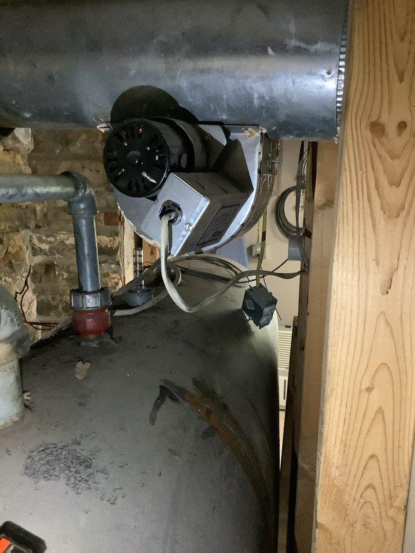 Inspected the boiler and exhaust system for reported water leak and found condensate at the flue outlet, with heavy corrosion and scale deposits inside the vent collar, including a pinhole perforation, and rust staining on the draft inducer area and appliance top. Documented the corroded venting and inducer assembly condition, and noted that the upstairs shower leak persists at a reduced rate and will require further evaluation.