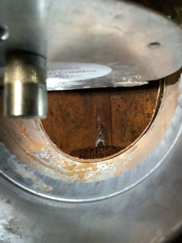 Inspected the boiler and exhaust system for reported water leak and found condensate at the flue outlet, with heavy corrosion and scale deposits inside the vent collar, including a pinhole perforation, and rust staining on the draft inducer area and appliance top. Documented the corroded venting and inducer assembly condition, and noted that the upstairs shower leak persists at a reduced rate and will require further evaluation.
