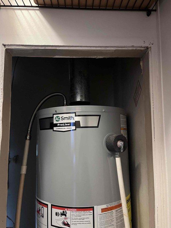 # Job Summary

Successfully installed A.O. Smith ProLine tanked water heater with all required connections and safety components.

# Work Performed

Installed new A.O. Smith ProLine commercial-grade water heater in recessed utility alcove. Connected hot and cold water supply lines using flexible connectors to ensure proper water flow. Installed pressure relief valve with discharge pipe routed according to code requirements. Attached expansion tank to right side of unit to manage thermal expansion and protect plumbing system. Connected black flexible vent pipe from top of unit extending vertically through ceiling for proper exhaust ventilation. Verified all connections for leaks and proper operation. Ensured all manufacturer warning labels and specification tags remained visible and intact per safety regulations. Tested unit for proper ignition, heating function, and temperature control. Confirmed pressure relief valve operation and discharge pipe positioning meets code standards. Recon