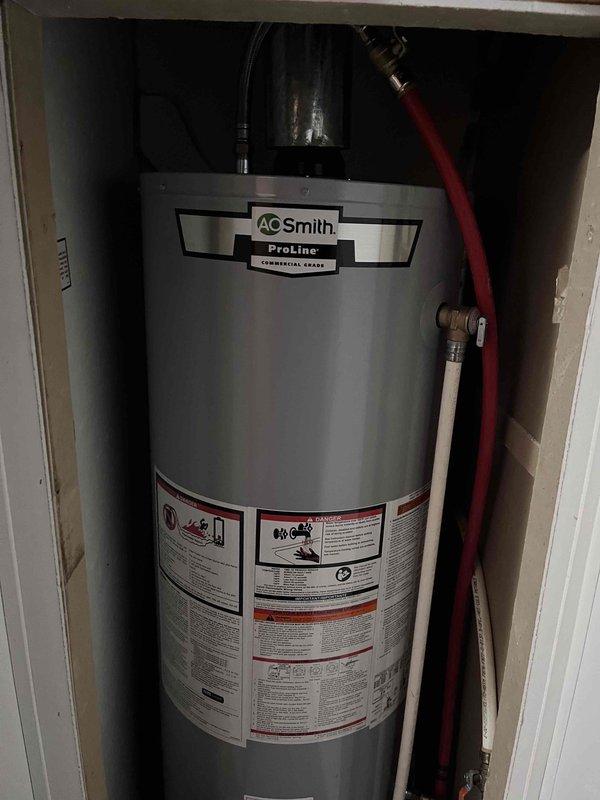 # Plumbing Service Report: Tanked Water Heater Installation

## Summary
Successfully completed installation of AO Smith ProLine commercial-grade tanked water heater in residential utility closet with all necessary plumbing connections, venting components, and safety equipment per manufacturer specifications and local code requirements.

## Work Performed

Installed new AO Smith ProLine commercial-grade water heater in confined utility closet space. Positioned unit on approved drain pan to protect surrounding area from potential water damage. Connected gas supply line using appropriate black pipe fittings at top of unit for safe fuel delivery. Installed hot water distribution line with red-coded copper piping along right side of tank, ensuring proper connection to household plumbing system. Configured cold water supply inlet with required shutoff valve for maintenance access.

Established proper venting system using black cylindrical components at tank crown to safely exhaust combustion