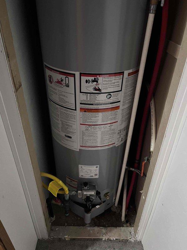 # Plumbing Service Report: Tanked Water Heater Installation

## Summary
Successfully completed installation of AO Smith ProLine commercial-grade tanked water heater in residential utility closet with all necessary plumbing connections, venting components, and safety equipment per manufacturer specifications and local code requirements.

## Work Performed

Installed new AO Smith ProLine commercial-grade water heater in confined utility closet space. Positioned unit on approved drain pan to protect surrounding area from potential water damage. Connected gas supply line using appropriate black pipe fittings at top of unit for safe fuel delivery. Installed hot water distribution line with red-coded copper piping along right side of tank, ensuring proper connection to household plumbing system. Configured cold water supply inlet with required shutoff valve for maintenance access.

Established proper venting system using black cylindrical components at tank crown to safely exhaust combustion