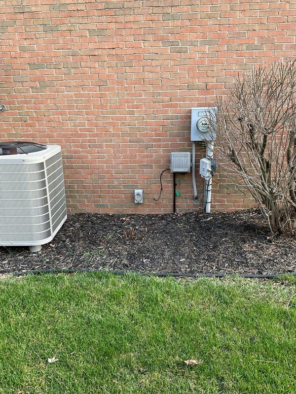 Conducted comprehensive site assessment for whole home generator installation at residential property. Evaluated existing electrical infrastructure including main service panel, meter base, and exterior utility connections to determine compatibility and capacity for generator integration. Documented current electrical panel configuration with multiple 220V circuits for range, HVAC, and appliances. Assessed optimal generator placement location adjacent to existing HVAC equipment on exterior brick wall, considering access to natural gas supply, electrical service entry point, and code-compliant clearances. Identified existing conduit pathways and junction box locations for transfer switch installation and generator connection. Photographed electrical panel interior showing circuit breaker arrangement and available capacity for automatic transfer switch integration. Evaluated site conditions including adequate workspace in mulched area near utility installations and confirmed structural r