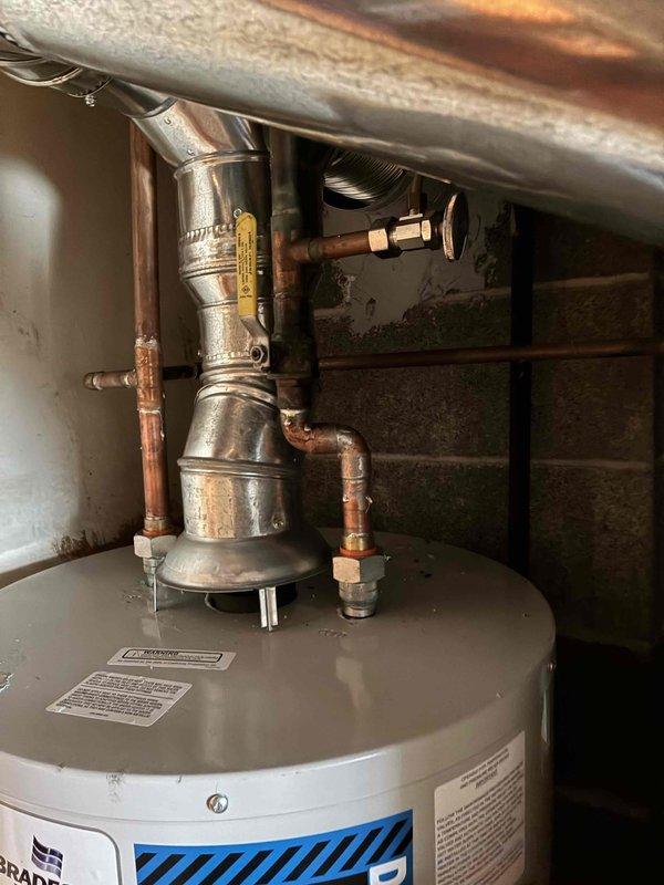 Installed Bradford White tanked water heater in basement utility area, connecting all copper supply lines and piping assemblies to the unit. Reconnected hot water distribution system with proper fittings, valves, and draft hood assembly, ensuring all connections were secure and operational per manufacturer specifications.