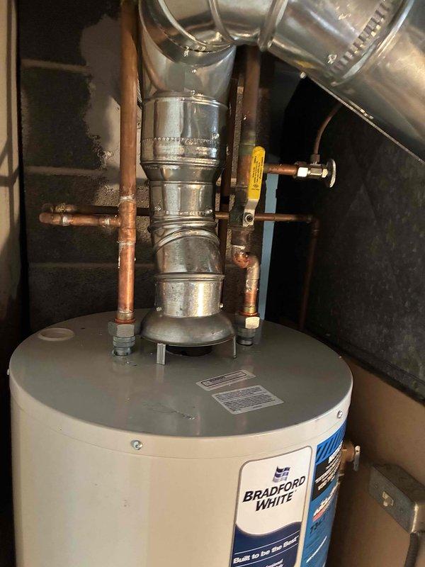 Installed Bradford White tanked water heater in basement utility area, connecting all copper supply lines and piping assemblies to the unit. Reconnected hot water distribution system with proper fittings, valves, and draft hood assembly, ensuring all connections were secure and operational per manufacturer specifications.