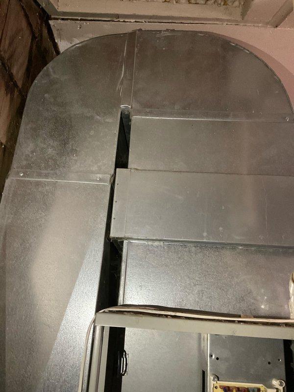 Conducted comprehensive assessment of existing HVAC system for replacement estimate. Evaluated aging furnace unit showing significant rust staining and corrosion on cabinet exterior, indicating prolonged water exposure and deterioration. Documented existing ductwork configuration in basement area, noting accumulated dust and age-related wear on rectangular sheet metal components with 90-degree elbow transitions. Photographed current equipment installation including copper refrigerant lines, electrical connections, and plumbing interfaces to develop accurate replacement specifications for three quoted system options.