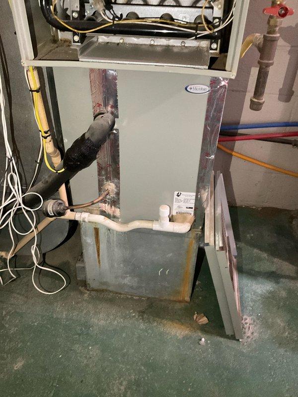 Conducted comprehensive assessment of existing HVAC system for replacement estimate. Evaluated aging furnace unit showing significant rust staining and corrosion on cabinet exterior, indicating prolonged water exposure and deterioration. Documented existing ductwork configuration in basement area, noting accumulated dust and age-related wear on rectangular sheet metal components with 90-degree elbow transitions. Photographed current equipment installation including copper refrigerant lines, electrical connections, and plumbing interfaces to develop accurate replacement specifications for three quoted system options.