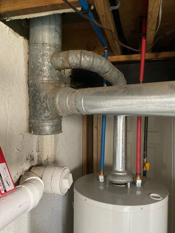 Completed comprehensive HVAC system assessment for quote 03591-02 System Estimate4-6, documenting existing furnace and ductwork configuration in basement utility area. Photographed current installation including aging galvanized metal ductwork system with visible moisture streaking and surface oxidation, existing furnace unit with connected supply and return ducts, and surrounding mechanical infrastructure including water heater and plumbing lines to provide accurate replacement specifications and equipment sizing requirements.