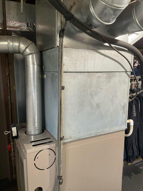 Completed comprehensive HVAC system assessment for quote 03591-02 System Estimate4-6, documenting existing furnace and ductwork configuration in basement utility area. Photographed current installation including aging galvanized metal ductwork system with visible moisture streaking and surface oxidation, existing furnace unit with connected supply and return ducts, and surrounding mechanical infrastructure including water heater and plumbing lines to provide accurate replacement specifications and equipment sizing requirements.