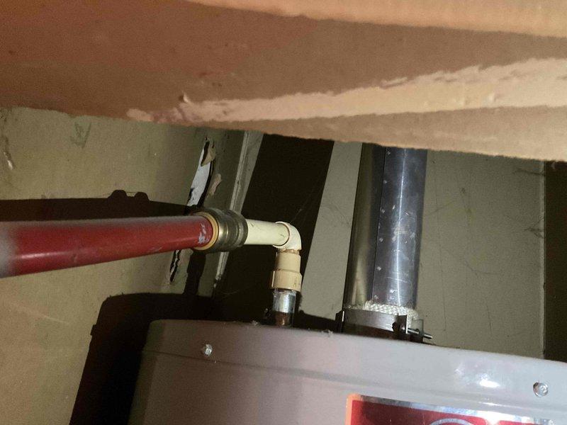 Completed water heater replacement estimate at mobile home park location. Assessed existing gas water heater installation including venting system, supply line connections, and spatial constraints within utility closet. Documented current configuration showing standard atmospheric vent water heater with metal flue pipe penetrating through ceiling, red-coded hot water supply piping with brass fittings and dielectric unions, CPVC cold water supply connections, and flexible aluminum vent duct work. Evaluated clearances, access points, and existing plumbing infrastructure to provide accurate replacement specifications and labor requirements.