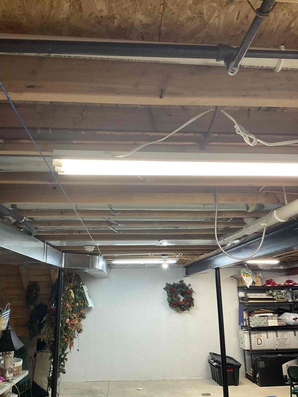 Conducted complimentary estimate for complete HVAC system replacement at residential property. Assessed existing outdoor air conditioning condenser unit with gray casing and black metal grid covering, mounted on concrete pad adjacent to building exterior with refrigerant lines and electrical conduit running along cream-colored brick wall. Evaluated basement heating system and existing infrastructure, noting exposed floor joists, ductwork routing, and current mechanical system layout. Provided comprehensive pricing options for new air conditioning unit and furnace replacement to meet homeowner's comfort needs. Documented existing equipment conditions and installation requirements through photographic records of outdoor condenser unit positioning and basement mechanical space configuration.