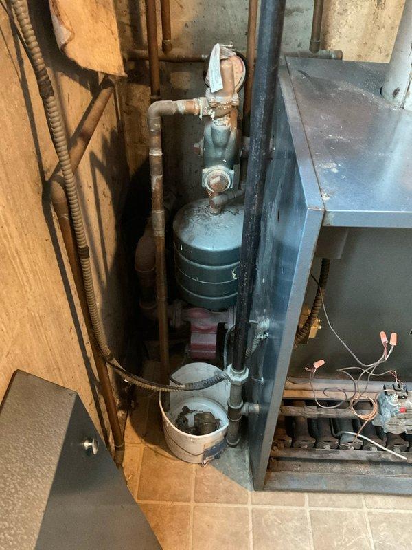Conducted on-site assessment for boiler replacement in basement utility area. Evaluated existing gray-blue painted boiler unit showing significant age-related deterioration, including dust accumulation on internal components, surface discoloration, and oxidation on associated cylindrical tank. Documented current system configuration including gas valve assembly, copper tubing connections, electrical wiring with wire connectors, and metallic flue pipe extending from unit top. Photographed open access panel revealing internal mechanical components and heating elements for replacement specifications. Prepared comprehensive replacement quote for complete boiler system upgrade with customer requesting expedited scheduling for morning installation window.