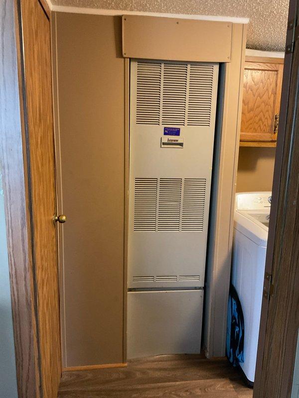 Completed site assessment for new air conditioning system installation at residential mobile home with no existing AC infrastructure. Evaluated electrical service panel and meter assembly in backyard to confirm adequate power supply capacity for new system installation. Inspected interior utility closet housing existing furnace/air handler unit to determine optimal placement and integration approach for new cooling equipment. Documented existing beige cabinet-style air handler with dual louver configuration and verified available space for refrigerant line routing and condensate drain installation. Assessed electrical service connections, outdoor condenser pad location requirements, and necessary modifications to accommodate complete split-system air conditioning installation.