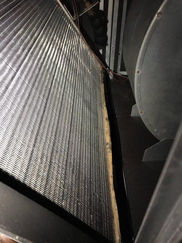 # HVAC Service Report - Unico System Insufficient Cooling

Responded to service call for Unico high-velocity air conditioning system not maintaining adequate cooling capacity. Upon arrival, performed visual inspection of air handling unit and evaporator coil assembly. Found significant dust and debris accumulation on evaporator coil fins, with visible brownish discoloration along bottom edge indicating restricted airflow and reduced heat transfer efficiency. Coil contamination was impacting system performance and preventing unit from achieving desired temperature setpoint.

Documented existing conditions with photographs showing extent of coil fouling and overall system condition. Evaporator coil displayed heavy buildup throughout fin surfaces, which restricts airflow across coil and diminishes cooling capacity. Copper refrigerant lines and surrounding components inspected and found intact with no visible damage or refrigerant leaks.

Recommended thorough coil cleaning to restore prope