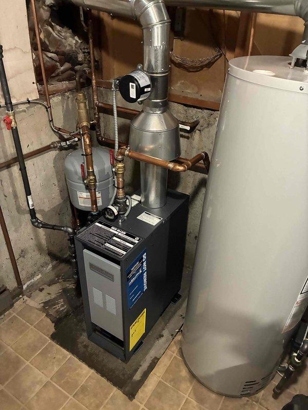 Completed full boiler installation in residential basement including mechanical, electrical, and venting connections. Installed new boiler unit with proper ductwork configuration featuring galvanized metal components and elbow joints, connected expansion tank with copper piping and brass fittings, and integrated system with existing water heater. All reconnections completed, system tested and operational.