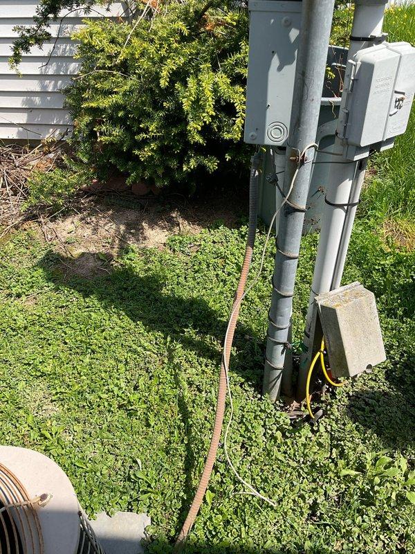 Conducted on-site evaluation for HVAC system replacement estimate. Documented existing outdoor condensing unit with copper-colored top grille and dark metal side panels, along with electrical meter installation and associated conduit routing on exterior wall. Recorded equipment model and serial numbers from furnace and air conditioning components for accurate replacement specifications and sizing calculations.