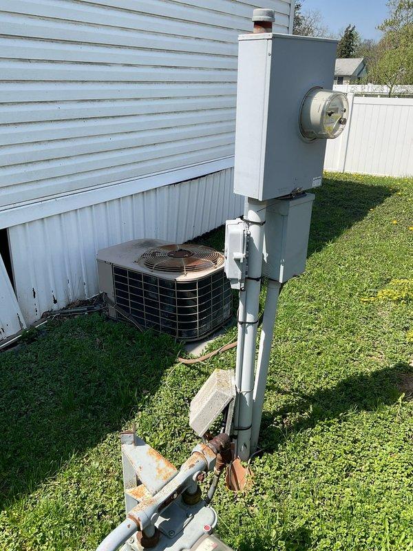 Conducted on-site evaluation for HVAC system replacement estimate. Documented existing outdoor condensing unit with copper-colored top grille and dark metal side panels, along with electrical meter installation and associated conduit routing on exterior wall. Recorded equipment model and serial numbers from furnace and air conditioning components for accurate replacement specifications and sizing calculations.