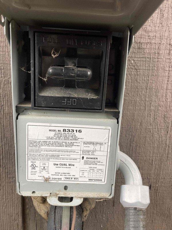 Completed preventive maintenance tune-up on HVAC system. Inspected electrical disconnect switch mounted on exterior wall, noting accumulation of cobwebs and dirt consistent with outdoor exposure. Verified disconnect switch operation and confirmed unit specifications on Model No. 83316 label. Performed voltage testing using digital multimeter, recording 49.99 volts at time of measurement to assess electrical performance and system functionality.