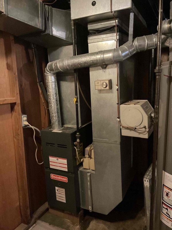 Performed comprehensive system evaluation of aging HVAC equipment including a 16-year-old Goodman furnace and 14-year-old air conditioning unit located in basement mechanical room. Assessed existing ductwork configuration, gas line connections, and electrical components. Documented current system condition through photographic documentation showing furnace cabinet, air handler, metal ductwork with moisture presence, and associated utility infrastructure. Provided complete system replacement estimate as alternative to repair options after determining equipment age and condition warranted full replacement consideration.