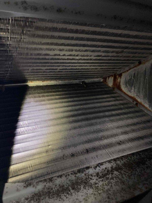 Completed preventive maintenance inspection on air conditioning system under Club AC8-12 agreement. Inspected dual-run capacitor rated at 45/5 μF, 440VAC, confirmed proper electrical connections and secure mounting. Observed evaporator coil with moderate to heavy dust and debris accumulation on fins, particularly concentrated in upper sections. Noted visible mold and mildew growth on interior surfaces and drain pan area, with moisture staining present on adjacent housing panels. System operational at time of inspection. Documented conditions with photographs for maintenance records.