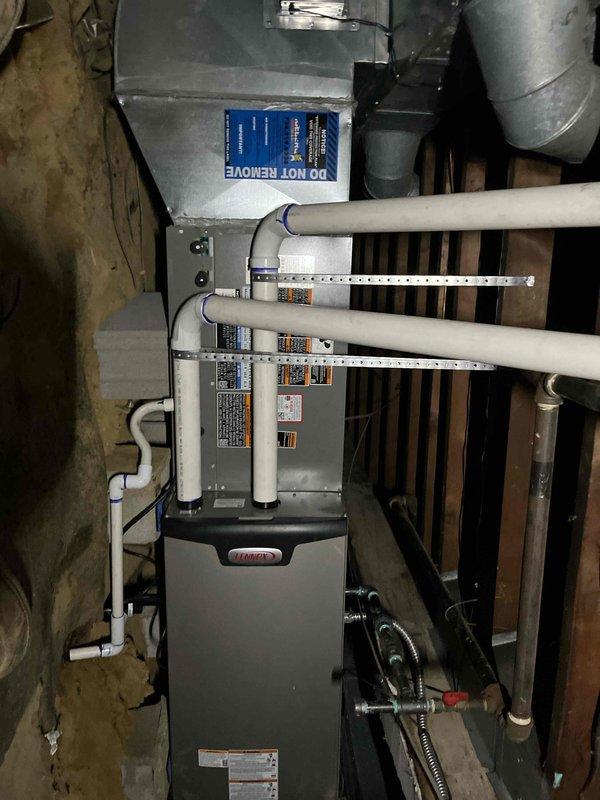 # HVAC Complete System Installation

Successfully completed a full HVAC system installation including new furnace and associated ductwork in basement mechanical space. Installed modern forced-air heating unit with proper venting configuration, utilizing dual PVC intake and exhaust pipes with appropriate support brackets and elbow fittings. Connected unit to existing ductwork infrastructure with metal duct transitions at upper portion of installation. Secured all electrical connections using flexible metal conduit, properly fastened and routed to unit. Ensured all manufacturer specification labels and safety warnings remain visible and accessible on furnace front panel. Installation includes proper clearances from wooden framing and structural elements per code requirements. All piping connections secured with appropriate fasteners and support hardware. System positioned on concrete floor with adequate access for future maintenance and service. Installation financed through approved fin