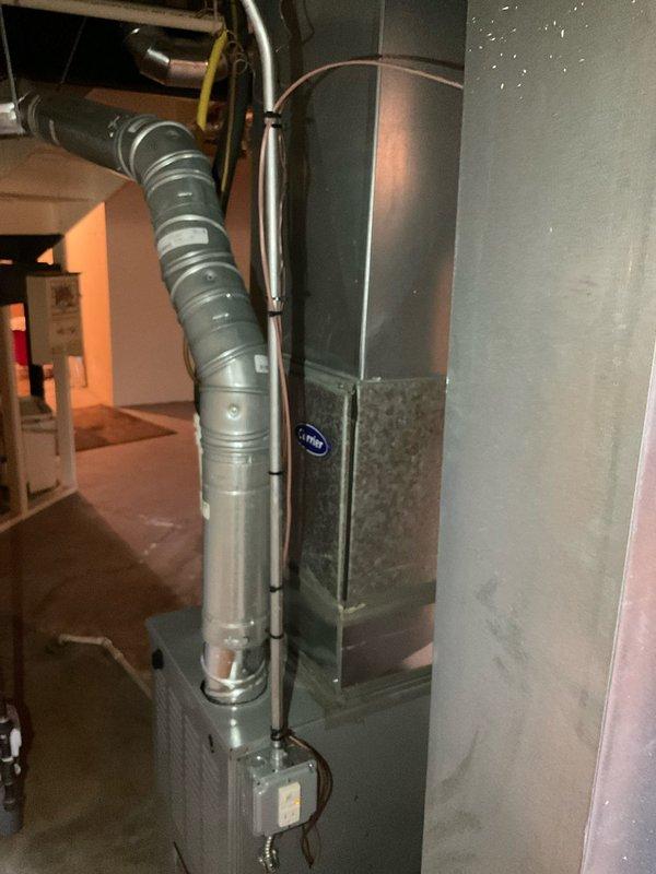 Conducted on-site evaluation for air conditioning system replacement estimate. Assessed existing Carrier HVAC equipment installation in basement utility area, documenting current system configuration including furnace/air handler unit, flexible ductwork connections, and rigid conduit routing. Photographed equipment condition and surrounding infrastructure to support replacement proposal specifications.