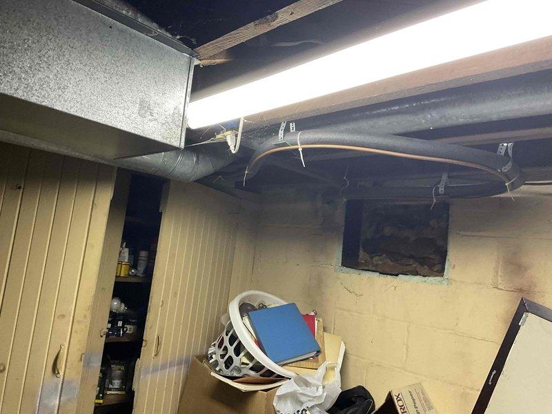 Completed HVAC estimate for Club AC12-2 replacement system in basement utility area. Assessed existing ductwork configuration including circular ventilation ducts, flexible silver ductwork, and corrugated metal conduit throughout exposed ceiling joists. Documented current mechanical installations with copper piping connections, PVC plumbing lines with valve assemblies, and cylindrical HVAC components mounted on concrete block walls. Identified ice formation on overhead piping indicating potential condensation issues and temperature control concerns requiring attention during replacement installation.