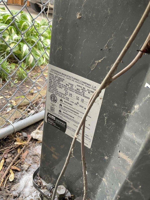 Responded to no cooling complaint on Goodman AC unit. Upon arrival, performed diagnostic inspection of outdoor condensing unit. Visually inspected equipment exterior, verified manufacturer labeling and unit specifications. Documented current condition of equipment showing normal environmental weathering. Checked electrical connections and observed wiring configuration at outdoor unit. Unit assessed as part of agreement visit maintenance protocol.