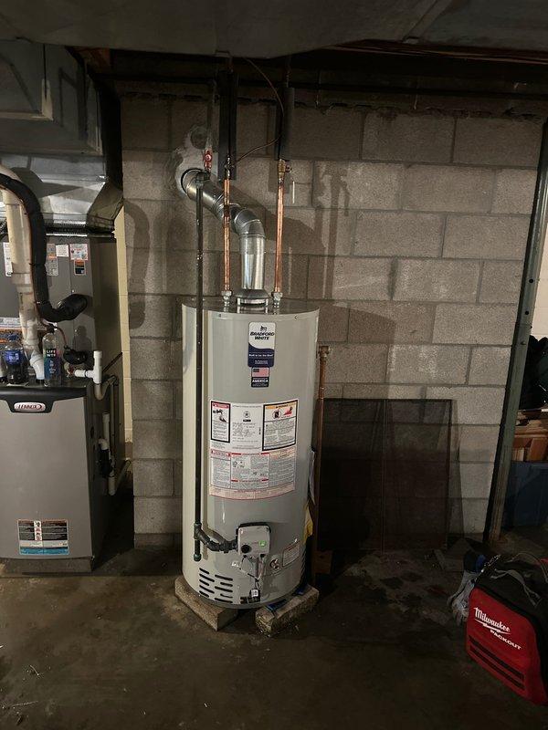 Completed installation of new Bradford White tanked water heater in basement utility area. Removed existing unit and positioned new water heater on platform per manufacturer specifications. Connected hot and cold water supply lines using copper piping with proper compression fittings. Installed galvanized metal flue vent pipe with 90-degree elbow configuration for proper exhaust ventilation. Verified all connections for proper seal and tested unit operation to ensure functionality. Installation meets professional standards with clean piping runs and secure mounting. Service financed and documentation on file.