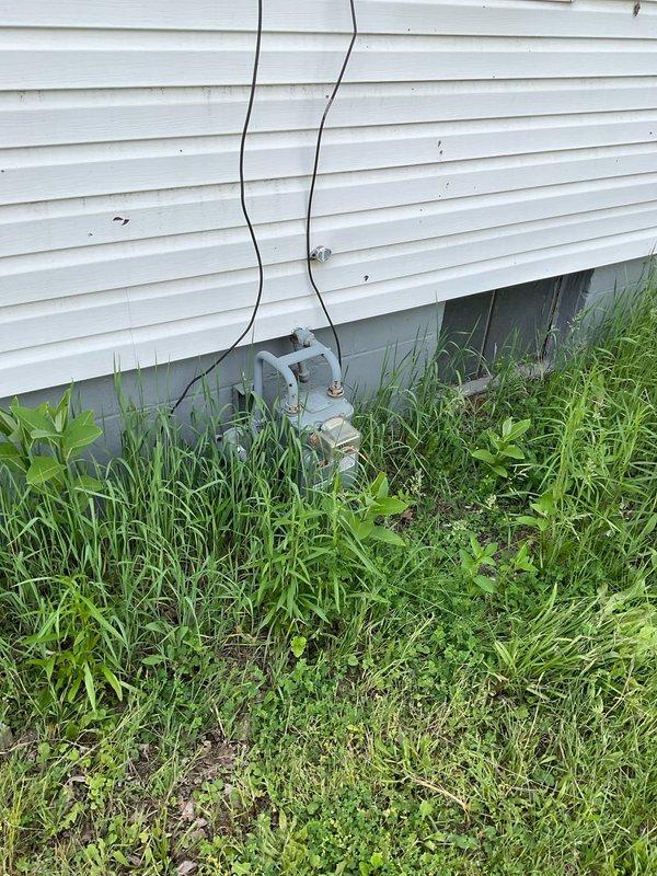 Conducted on-site assessment of existing outdoor air conditioning condenser unit for replacement estimate. Documented current system configuration including beige/tan condenser with spiral fan grille positioned against exterior wall with electrical disconnect boxes and wiring. Evaluated unit accessibility and noted vegetation overgrowth around equipment base requiring clearance for proper airflow and service access. Provided comprehensive estimate options for single component AC replacement and complete system replacement to address customer's cooling needs.