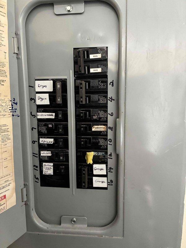 Conducted comprehensive site evaluation for complete HVAC system replacement at residential property. Documented existing outdoor condensing unit with standard configuration including white top cover, circular fan grille, and protective black metal side panels. Unit currently positioned on grade-level installation with direct wall mounting and electrical disconnect box present. Assessed electrical service panel containing dual-row circuit breaker configuration with labeled circuits for proper system integration planning. Evaluated existing refrigerant line set routing, condensate drainage pathway, and electrical conduit runs from exterior unit to main panel. Inspected clearance requirements around outdoor equipment, noting adequate space from landscaping and building structure for proper airflow and service access. Prepared detailed estimate documentation for 10-12 ton system replacement including equipment specifications, installation requirements, and necessary electrical modificatio