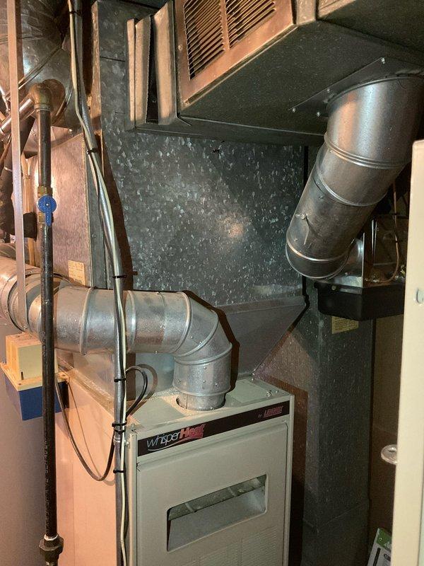 Conducted on-site evaluation of existing HVAC system for replacement estimate. Documented current Wright-branded furnace installation in basement mechanical room, including connected galvanized ductwork, air handler configuration, and spatial constraints. Photographed equipment specifications, duct routing, clearances, and surrounding utilities including plumbing and electrical components to develop comprehensive replacement proposal for complete system upgrade.