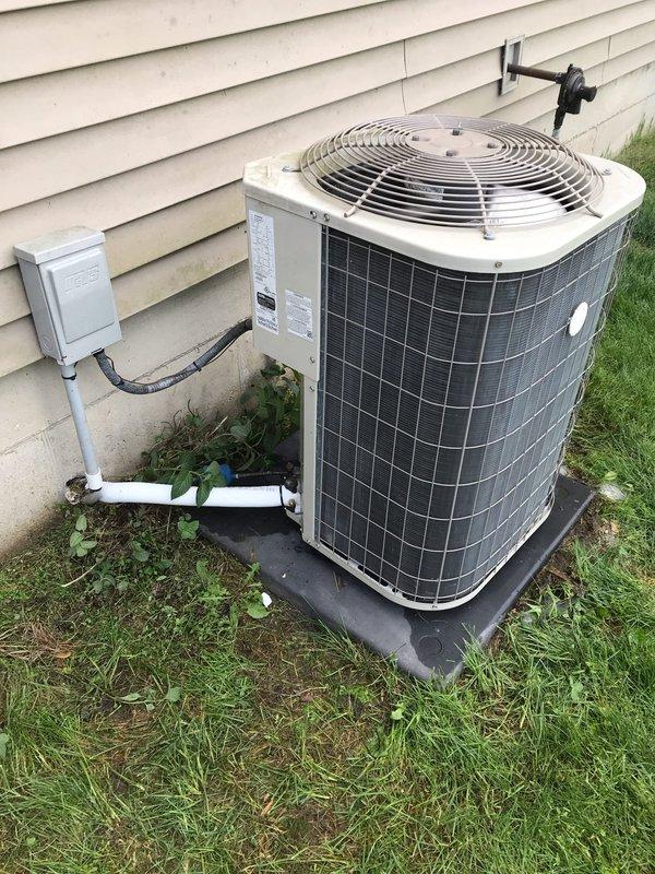 Conducted club maintenance follow-up visit to assess outdoor condensing unit and provide guidance on repair versus replacement options. Documented current system condition through comprehensive photography, capturing unit positioning on rubber isolation pad, electrical disconnect and conduit connections, refrigerant line routing with wall-mounted brackets, and PVC condensate drainage configuration. Unit appears operational with standard outdoor weathering; vegetation growth noted around base requiring clearance maintenance for optimal airflow and efficiency.