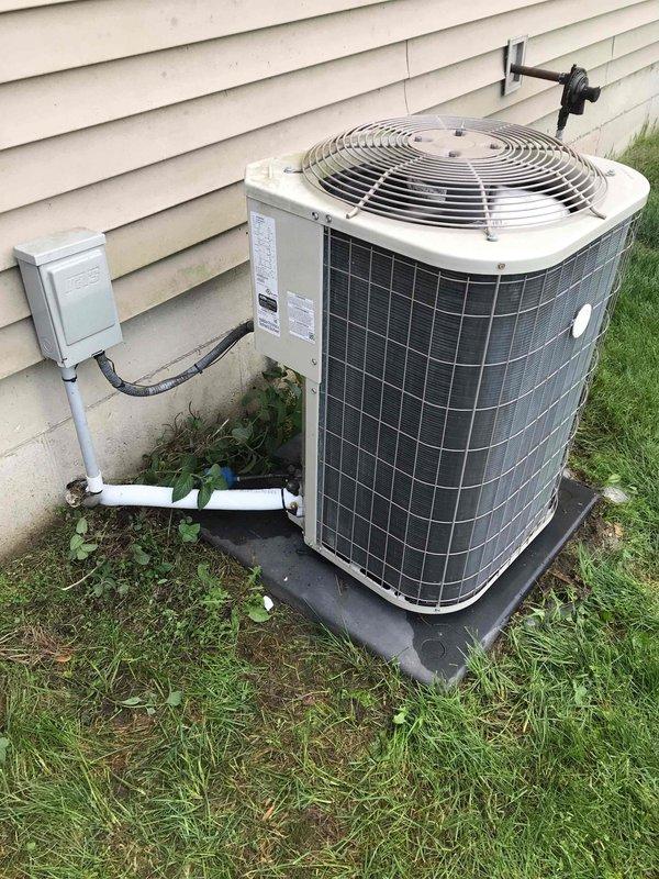 Conducted club maintenance follow-up visit to assess outdoor condensing unit and provide guidance on repair versus replacement options. Documented current system condition through comprehensive photography, capturing unit positioning on rubber isolation pad, electrical disconnect and conduit connections, refrigerant line routing with wall-mounted brackets, and PVC condensate drainage configuration. Unit appears operational with standard outdoor weathering; vegetation growth noted around base requiring clearance maintenance for optimal airflow and efficiency.