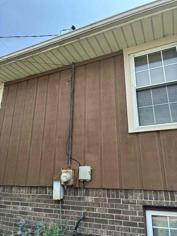 Provided estimate for complete air conditioning system replacement on 25-year-old non-operational unit located at exterior of residence. Assessed existing outdoor condenser unit mounted on concrete pad with overgrown vegetation requiring clearance, evaluated electrical service components including meter, disconnect, and conduit routing along brown siding and brick exterior wall. Quoted replacement system compatible with existing natural gas furnace infrastructure.