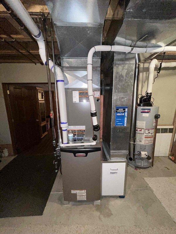 Completed full HVAC system installation in basement mechanical room, including 110,000 BTU gas furnace with PVC venting, 4-ton air conditioning condenser unit positioned on left side of residence, and whole-home humidifier integration. Condenser installed on composite pad with proper drainage stone bedding, all refrigerant lines connected and charged to manufacturer specifications. System tested and operational with all ductwork connections secured and financing documentation processed through Michigan Saves program.