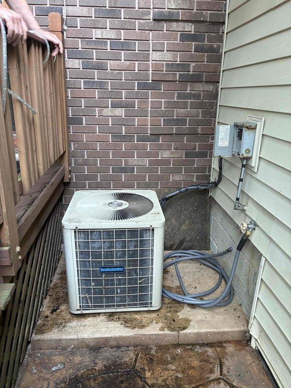 Conducted on-site evaluation of existing outdoor air conditioning condenser unit located in confined side yard area between structures. Assessed current equipment condition, electrical disconnect configuration, and meter placement for replacement feasibility. Documented unit positioning on concrete pad, clearance constraints imposed by brick wall, vinyl siding, and wooden fence, along with existing electrical conduit routing from distribution boxes to support comprehensive replacement estimate.