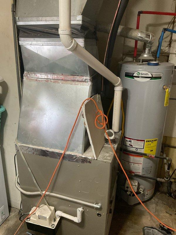 Conducted on-site evaluation for air conditioning system installation estimate at residence currently equipped with gas furnace only. Assessed existing HVAC infrastructure including gray cabinet-style furnace unit with PVC condensate drainage system located in basement utility area. Evaluated available space, electrical requirements, and ductwork configuration to determine optimal placement and sizing for new AC system. Documented existing equipment layout including water heater proximity and clearance requirements for future outdoor condenser unit installation and indoor evaporator coil integration with current forced-air heating system.