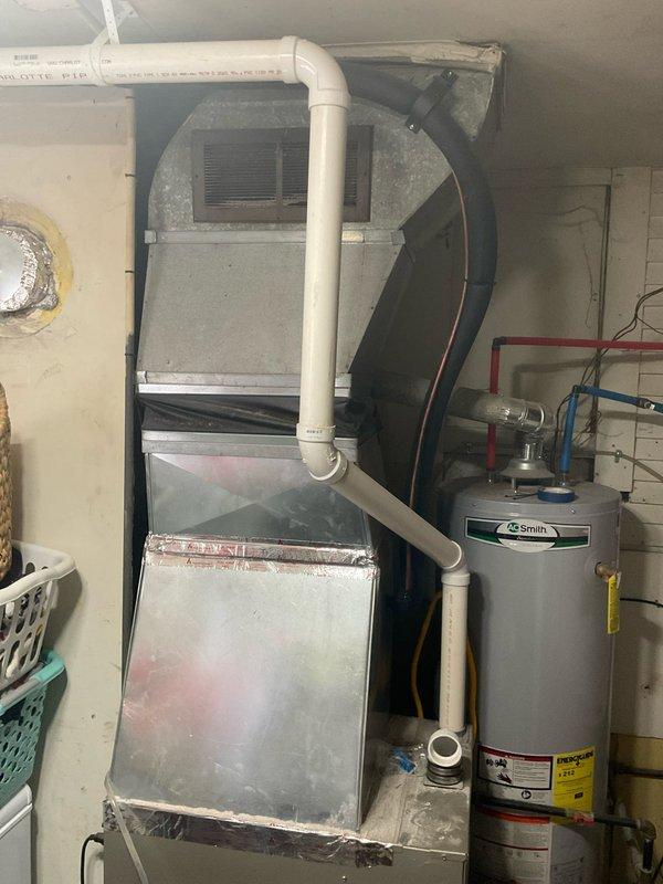 Conducted on-site evaluation for air conditioning system installation estimate at residence currently equipped with gas furnace only. Assessed existing HVAC infrastructure including gray cabinet-style furnace unit with PVC condensate drainage system located in basement utility area. Evaluated available space, electrical requirements, and ductwork configuration to determine optimal placement and sizing for new AC system. Documented existing equipment layout including water heater proximity and clearance requirements for future outdoor condenser unit installation and indoor evaporator coil integration with current forced-air heating system.