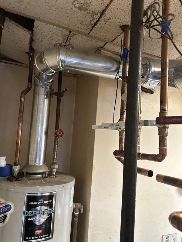Completed full boiler system installation in basement utility room, including mechanical, electrical, and flue liner components. Installed Bradford White Defender model water heater with metallic exhaust flue system featuring 90-degree elbow joint, secured with proper metal strapping for code compliance. Configured copper piping manifold with three vertical risers, installed brass ball valves on each line, and mounted white plastic mounting brackets for secure pipe support. Reconnected all plumbing distribution lines to existing copper infrastructure and verified proper water flow through system. Installed electrical connections and routed wiring along ceiling joists. All work completed to manufacturer specifications with system tested and operational upon completion.