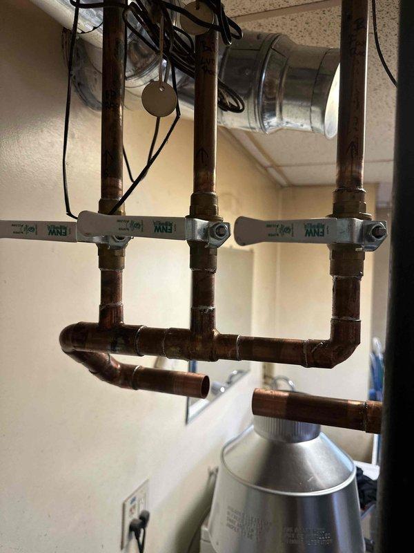 Completed full boiler system installation in basement utility room, including mechanical, electrical, and flue liner components. Installed Bradford White Defender model water heater with metallic exhaust flue system featuring 90-degree elbow joint, secured with proper metal strapping for code compliance. Configured copper piping manifold with three vertical risers, installed brass ball valves on each line, and mounted white plastic mounting brackets for secure pipe support. Reconnected all plumbing distribution lines to existing copper infrastructure and verified proper water flow through system. Installed electrical connections and routed wiring along ceiling joists. All work completed to manufacturer specifications with system tested and operational upon completion.