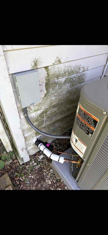 # HVAC Installation Summary

Successfully installed a 2-ton air conditioning system with matching evaporator coil at rear location of property. Installation included complete mechanical reconnection of refrigerant lines, electrical connections, and condensate drainage system. Unit was positioned on ground-level pad against exterior wall with proper clearances maintained. White PVC condensate drain line was installed and properly secured with appropriate fittings and connections. Black electrical conduit and refrigerant line set were run from outdoor condensing unit to indoor coil location. All connections were completed per manufacturer specifications and industry standards. System was tested and verified operational upon completion.